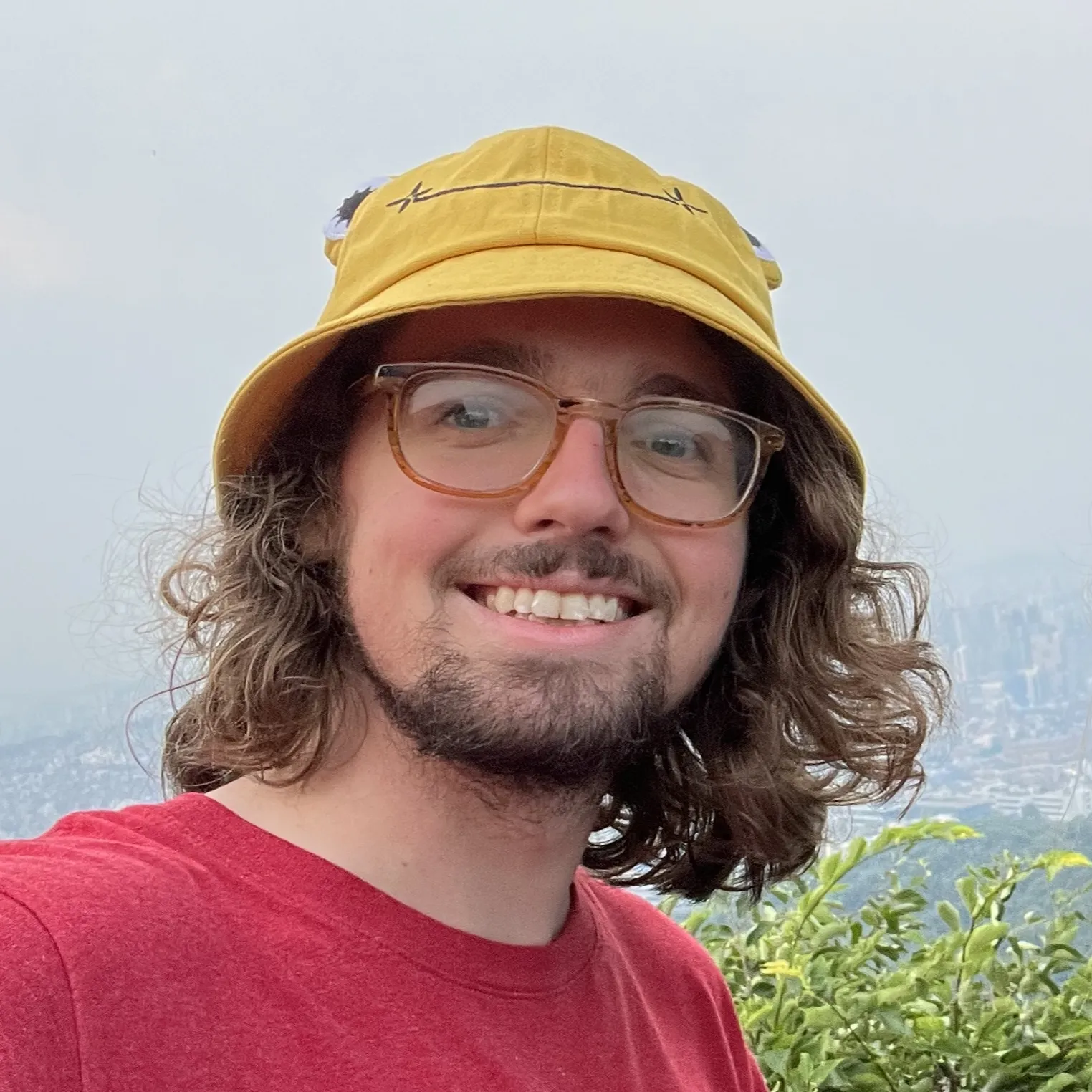 Myself smiling, wearing a yellow bucket hat and a red t-shirt